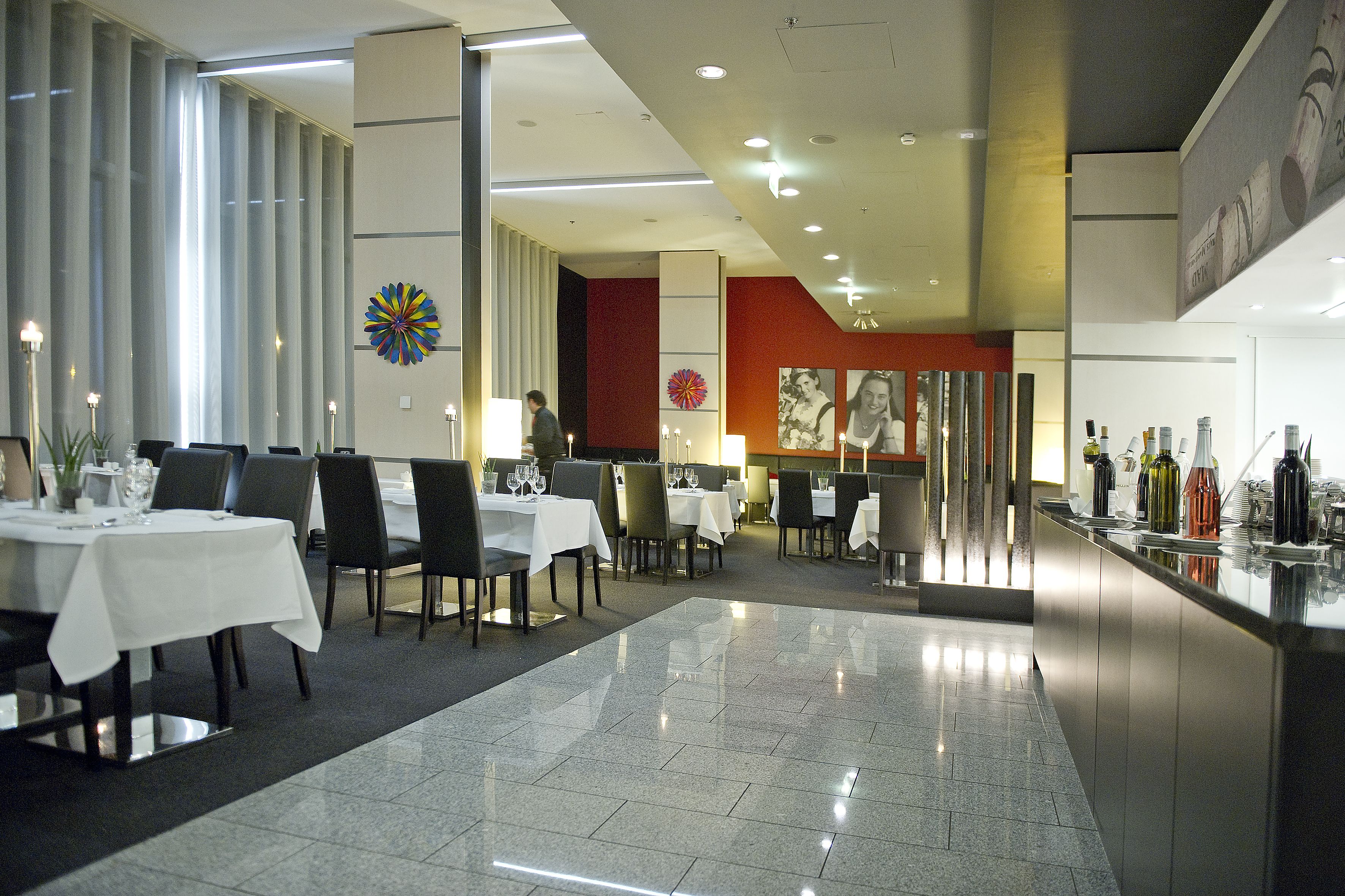 A modern restaurant with tables set for dining, a bar area, and a decorative wall with a colorful flower design.