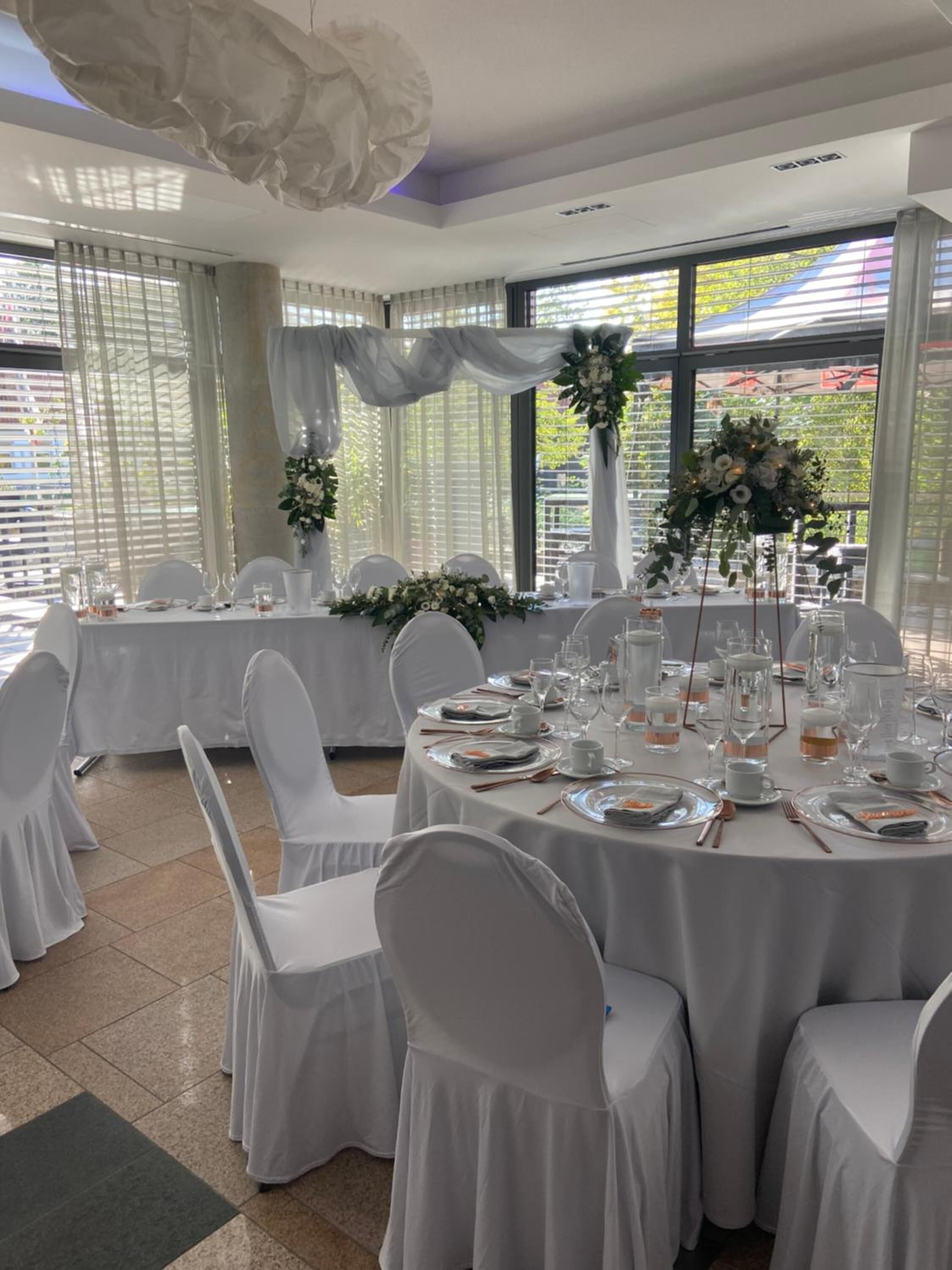 A banquet hall with round tables set for a formal event, featuring white tablecloths, chairs, and floral centerpieces.