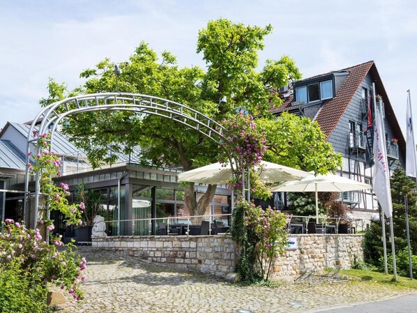 A restaurant with outdoor seating, stone walls, and a metal archway.