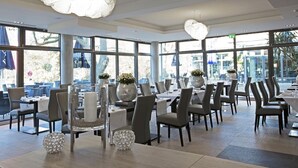 Un comedor moderno con amplios ventanales, mesas dispuestas con sillas y jarrones decorativos.