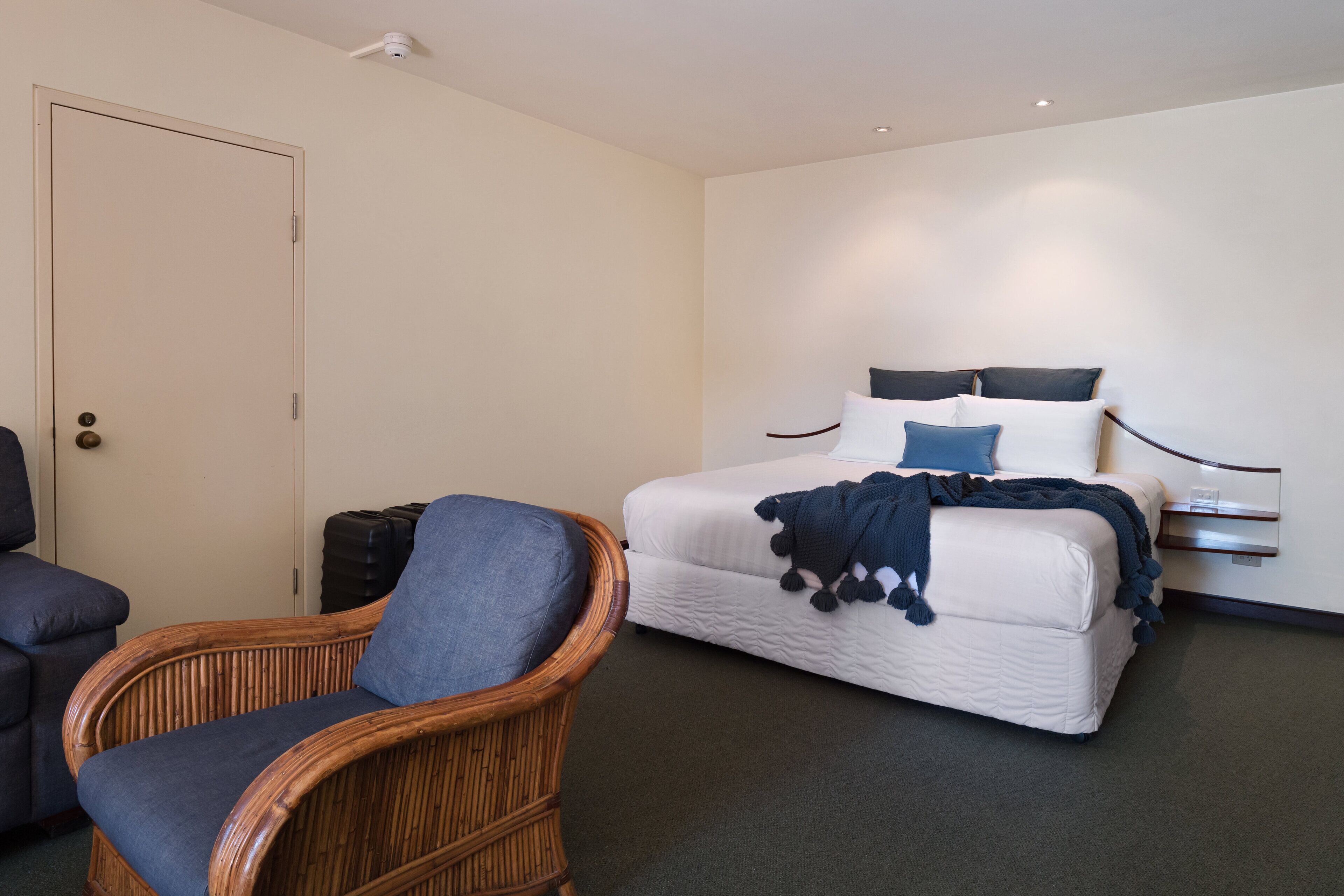 A hotel room with a bed, a chair, a wardrobe, and a door.