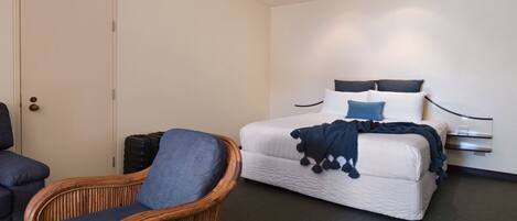 A hotel room with a bed, a chair, a wardrobe, and a door.