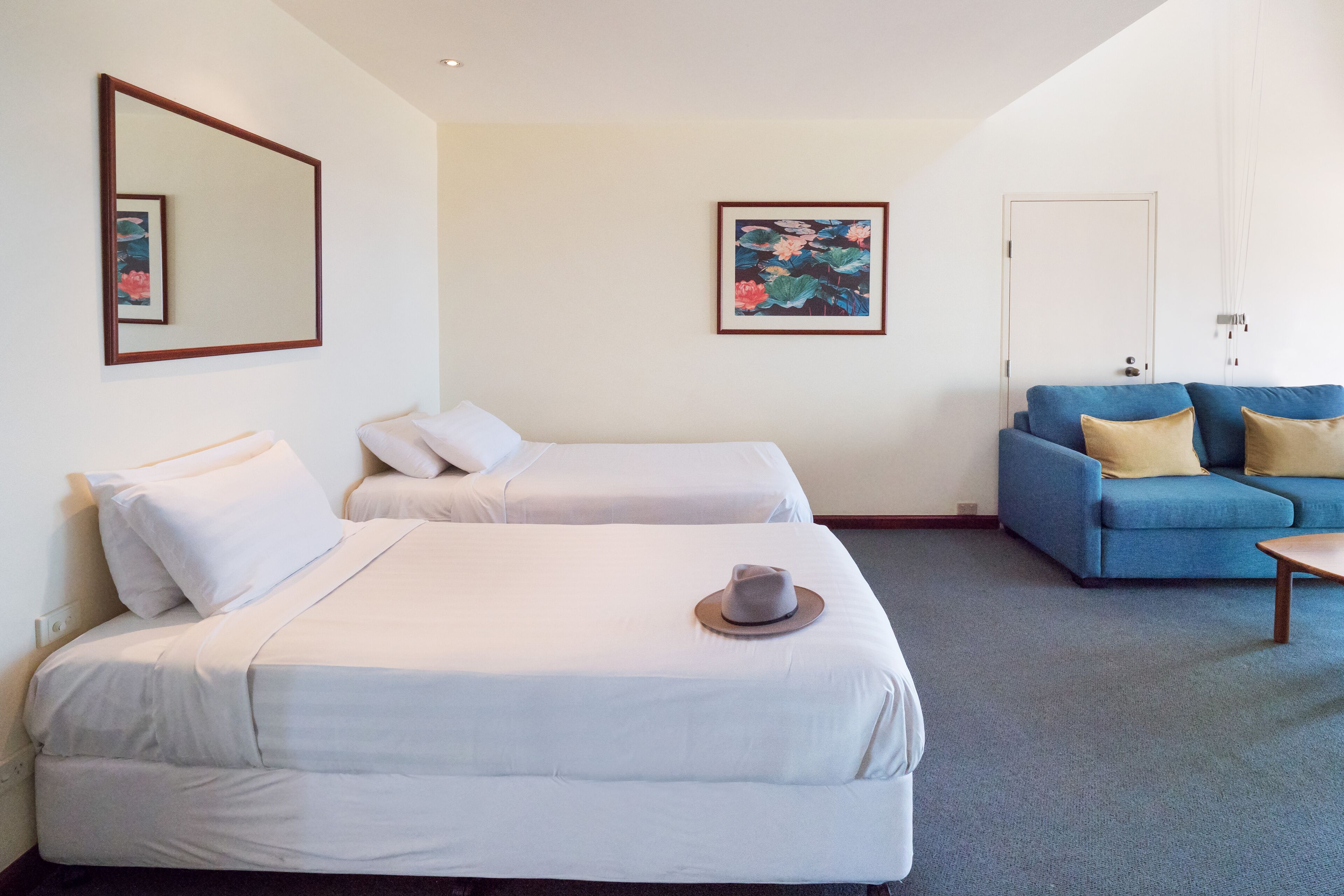 Een hotelkamer met twee bedden, een blauwe bank en een schilderij aan de muur.