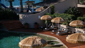 A pool area with thatched umbrellas, lounge chairs, and a view of the ocean. - Beach Hotel Resort (Byron Bay)