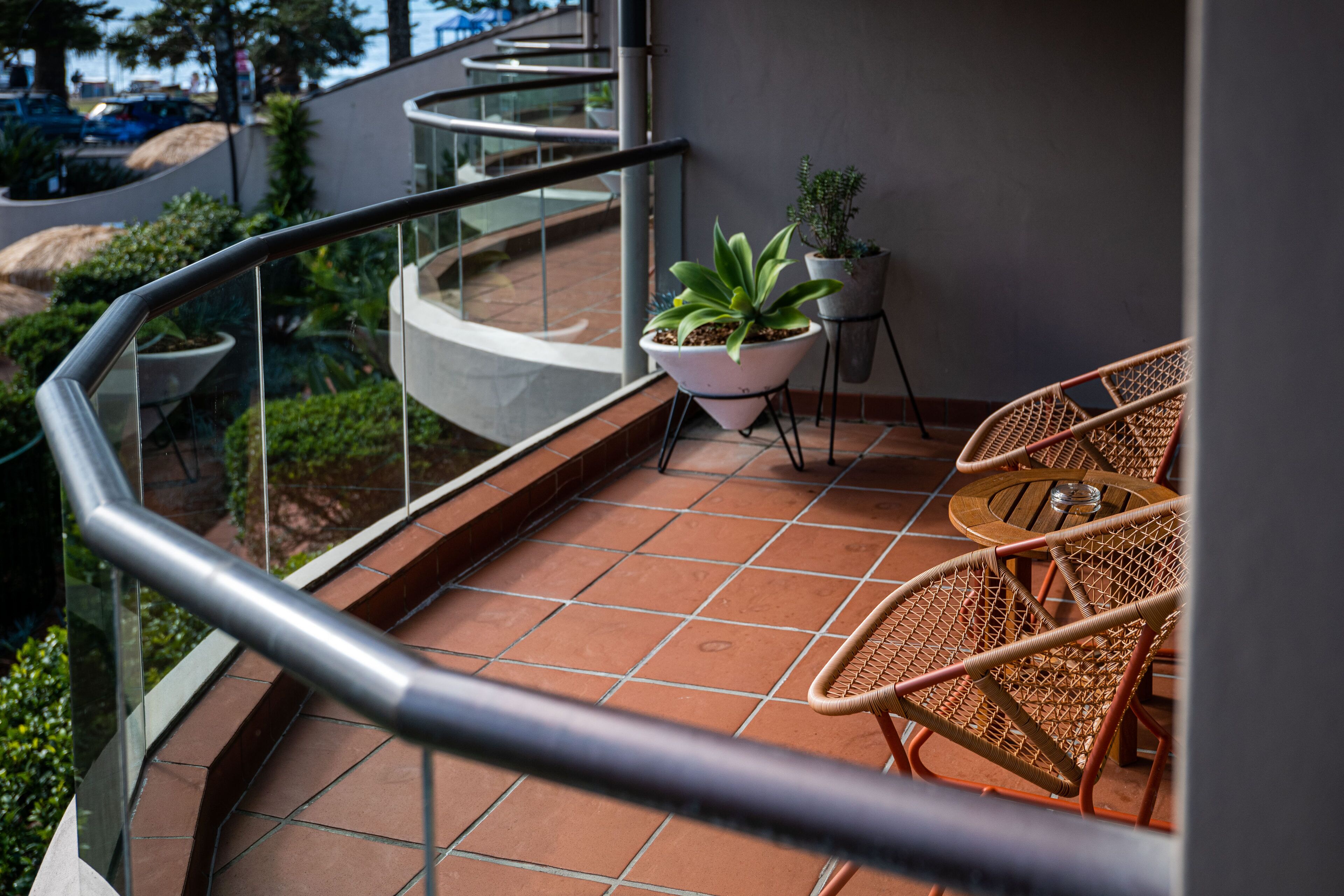 A balcony with wicker chairs and a potted plant, overlooking a landscaped area with a spiral staircase.