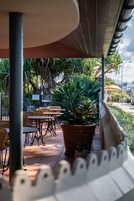An outdoor seating area with wicker chairs and tables, surrounded by potted plants and a wooden fence.