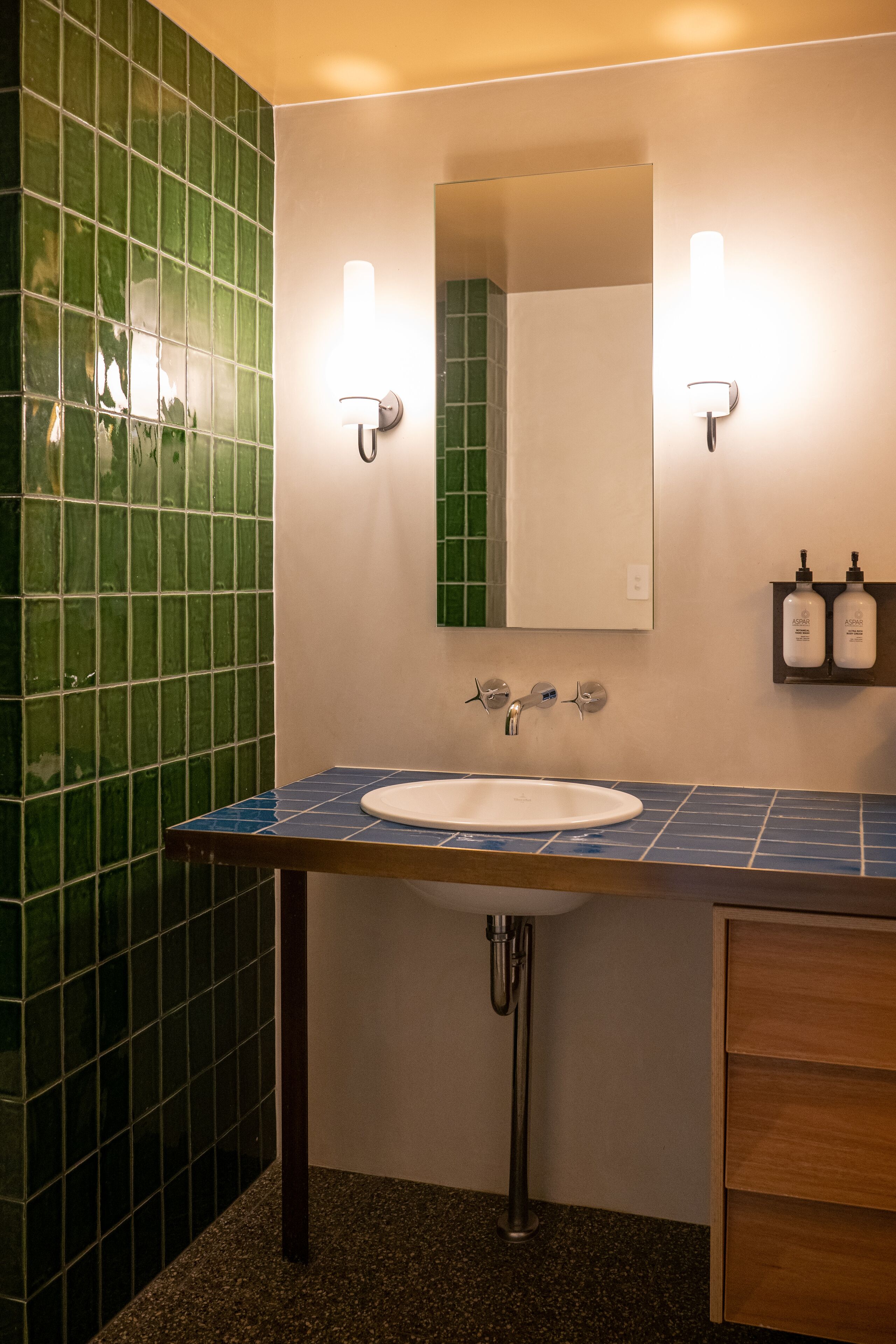 A bathroom with a white sink, green tiled walls, and two wall-mounted light fixtures.