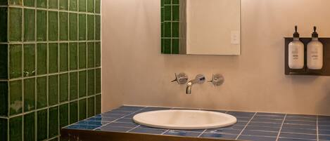 A bathroom with a white sink, green tiled walls, and two wall-mounted light fixtures.