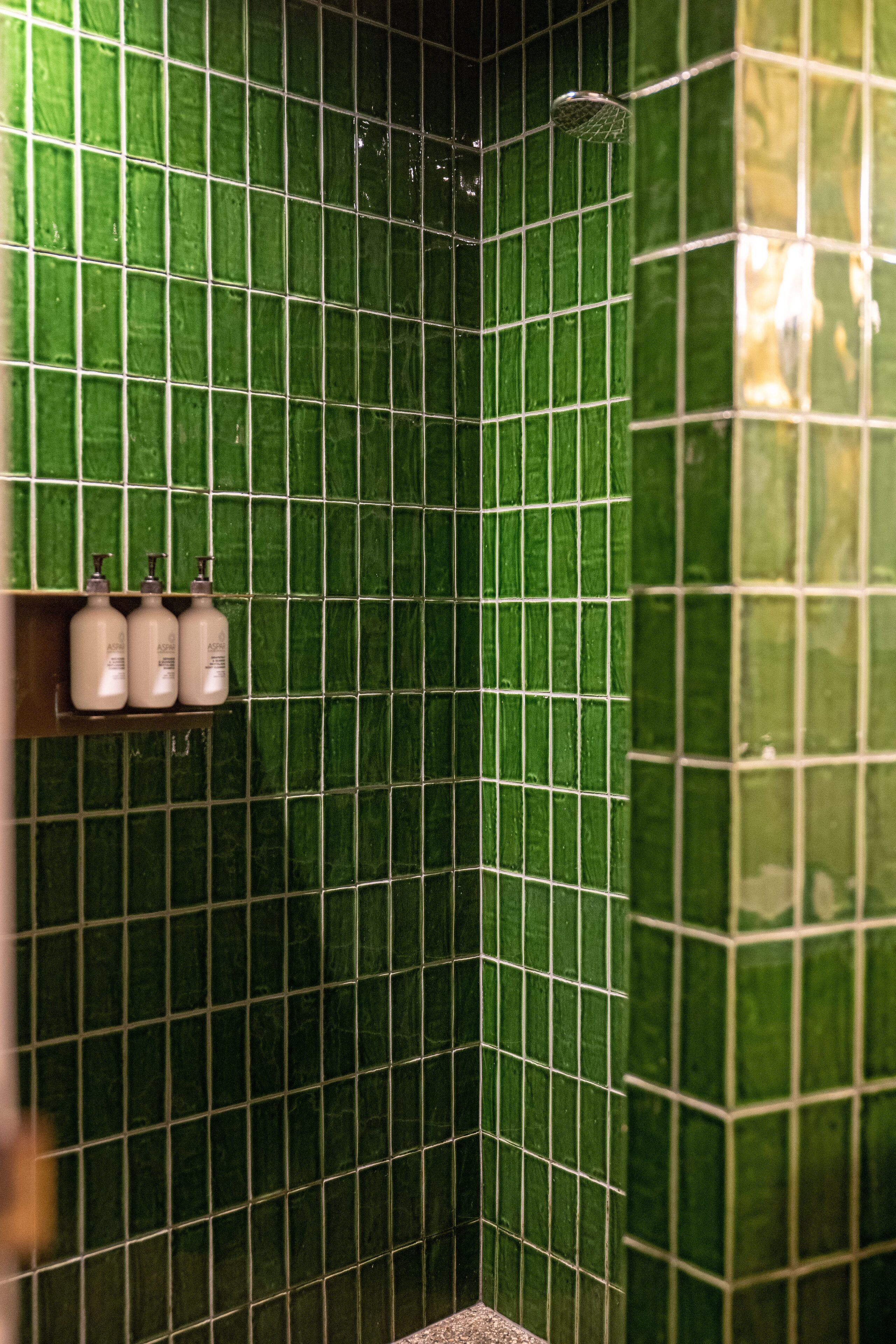 Zona de ducha con azulejos verdes y un estante con tres botellas.