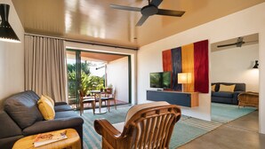 A modern living room with a sofa, a wooden chair, a TV on a low wall, and a dining area with a table and chairs. - Beach Hotel Resort (Byron Bay)