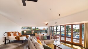 A modern living room with a sofa, a coffee table, and a dining table. There is a large window with a view of the outdoors. - Beach Hotel Resort (Byron Bay)