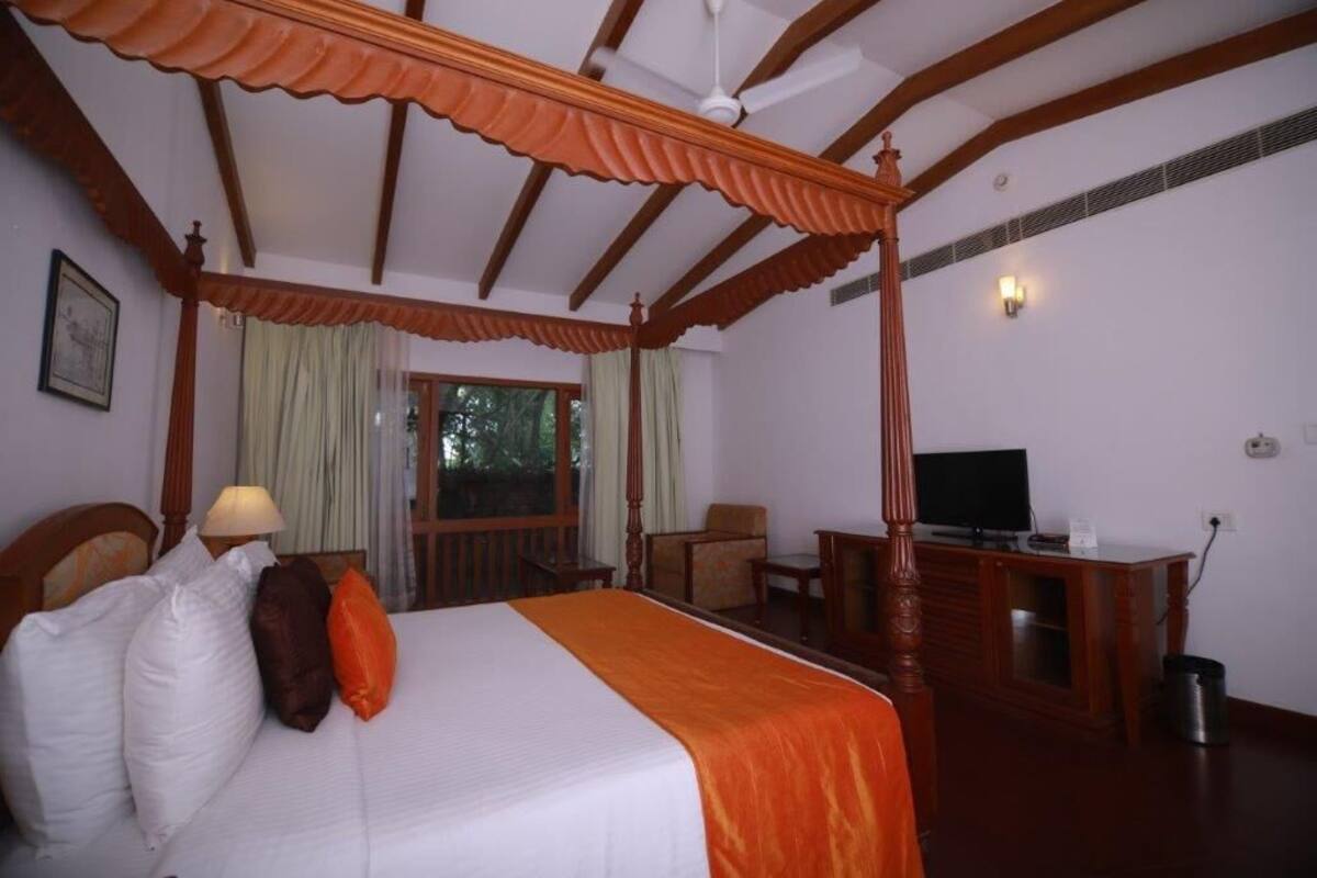 A four-poster bed with a television and desk in a room with wooden beams and a window.