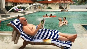 A man lying on a lounge chair by a pool, reading a book. - Lemon Tree Vembanad Lake Resort, Kerala (Cherthala)