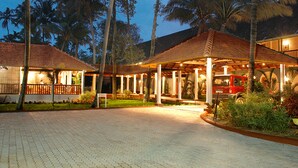 A hotel entrance with a paved driveway, covered outdoor seating area, and a red vehicle parked nearby. - Lemon Tree Vembanad Lake Resort, Kerala (Cherthala)