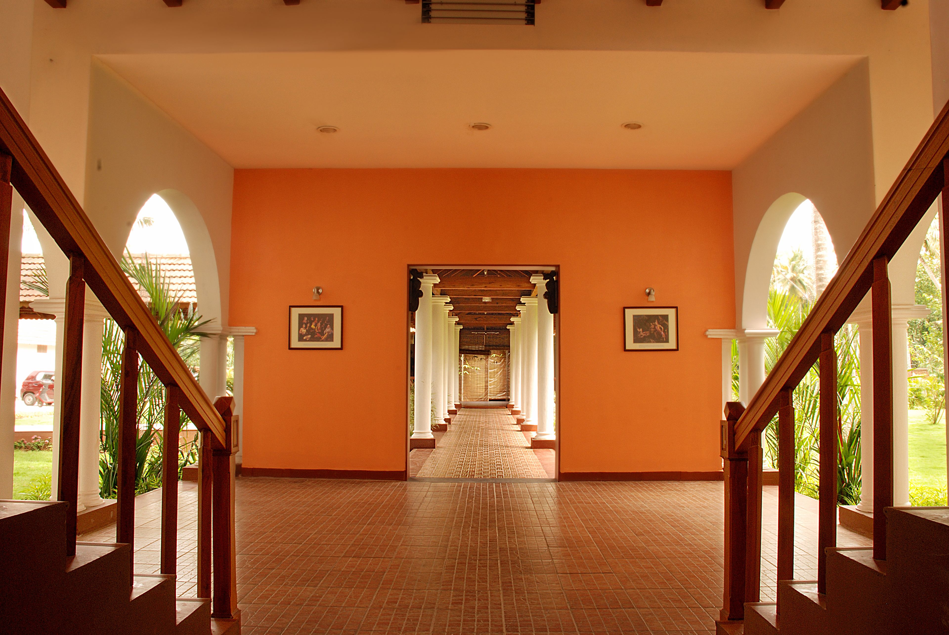 A corridor with a tiled floor, wooden railings, and framed pictures on the walls.