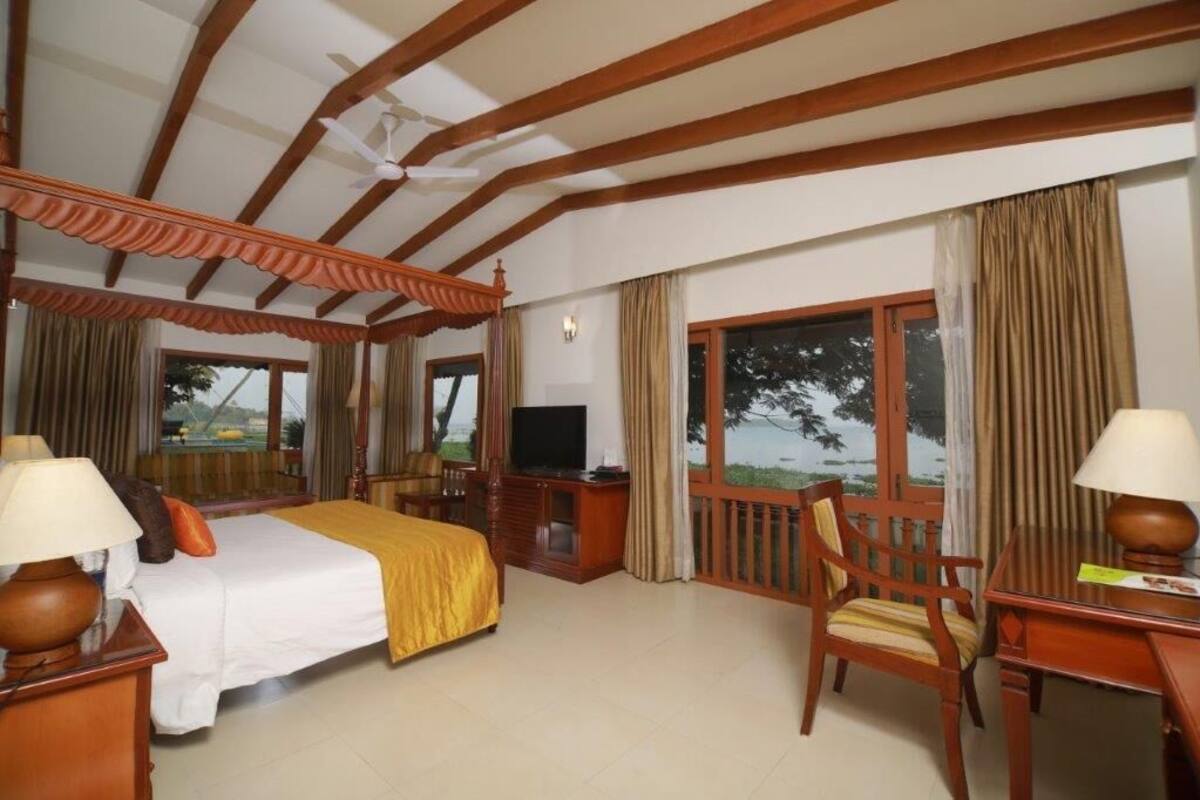 A hotel room with a bed, a desk, a chair, a television, and a balcony with curtains.