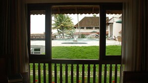 A view through a window with a white balustrade, a fountain, and a lawn with a palm tree. - Lemon Tree Vembanad Lake Resort, Kerala (Cherthala)