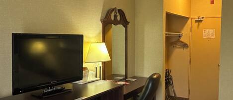 A hotel room with a bed, a desk with a television, a chair, a lamp, and a wardrobe.