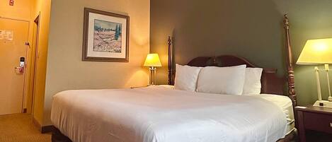 A hotel room with a large bed, a framed picture on the wall, a bedside lamp, and a door.