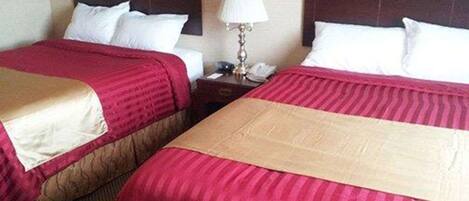 Habitación de hotel con dos camas, cada una con cubrecama rojo y beige, almohadas blancas y una mesita de noche con lámpara y teléfono.