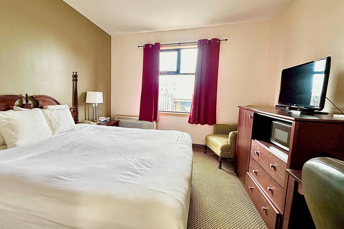 Habitación de hotel con una cama grande, televisión, escritorio con cajones, una silla y ventana con cortinas.