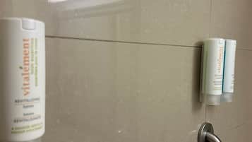 A bathroom with a hand dryer and two bottles of Revitalisant soap on the wall.