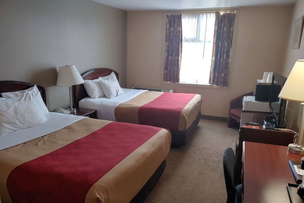 Habitación de hotel con dos camas, un escritorio, una silla, una lámpara, un teléfono y una ventana con cortinas.