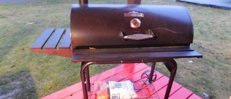 Un barbecue posé sur une table rouge, avec un sac de charbon de bois et un briquet à proximité.