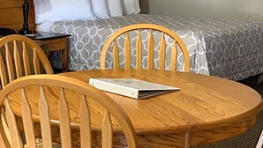 A hotel room with a wooden headboard, a bed with patterned bedding, a nightstand with a lamp, and a round wooden table with chairs. - Packwood Inn (Packwood)
