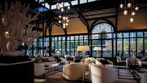 A spacious lobby with high ceilings, large windows, and modern furniture. - Grand Hôtel de Courtoisville (Saint-Malo)