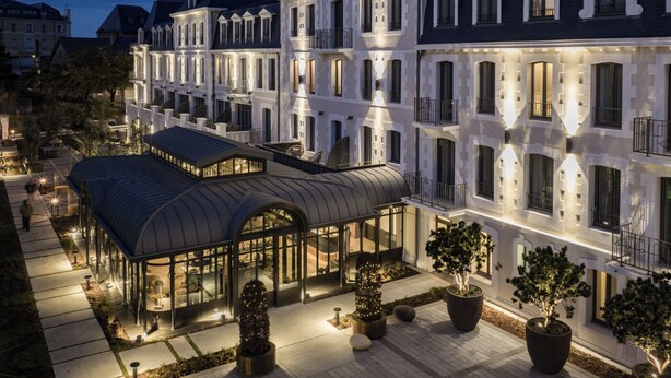 A multi-story hotel with a covered outdoor area, large windows, and potted plants. - Grand Hôtel de Courtoisville (Saint-Malo)