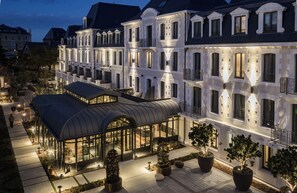 Un hotel de varios pisos con un espacio exterior cubierto, grandes ventanales y plantas en macetas.