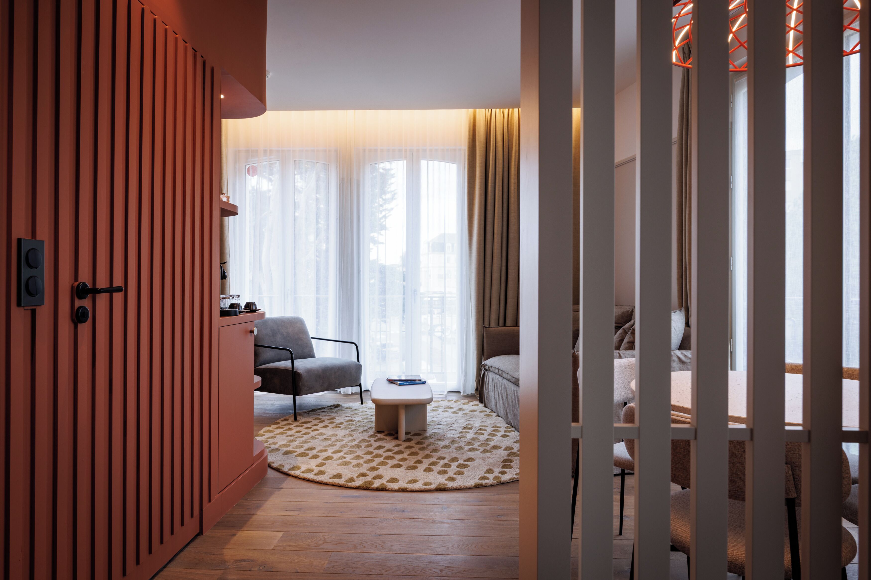 Una habitación con piso de madera, un tapete redondo, un sofá, una silla, una pequeña mesa y un aparador.