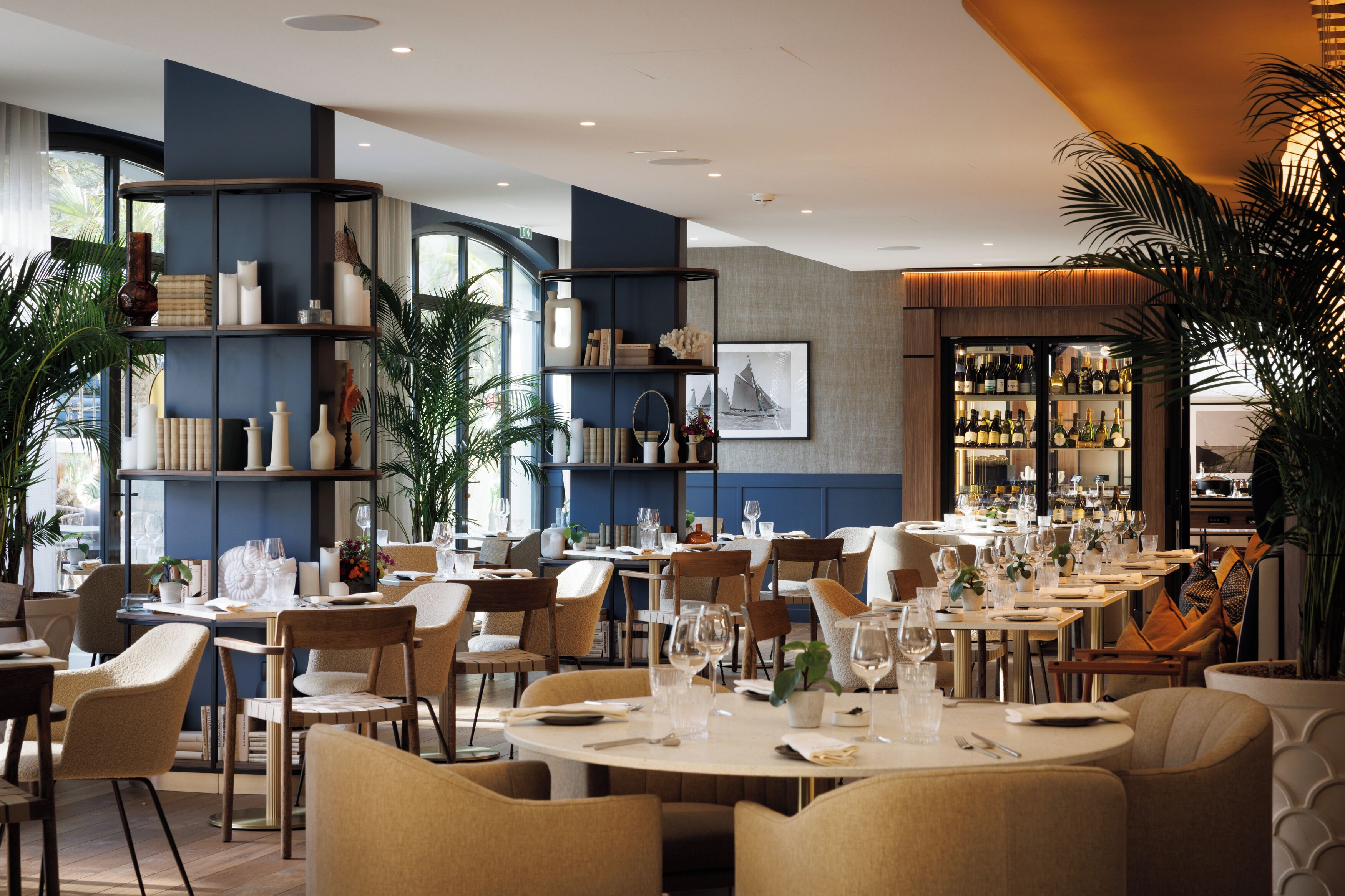 Un restaurante con mesas redondas, sillas y estanterías con objetos decorativos.