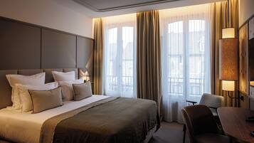 Habitación de hotel con una cama grande, un escritorio y una silla. Hay una ventana con cortinas y vistas a edificios.