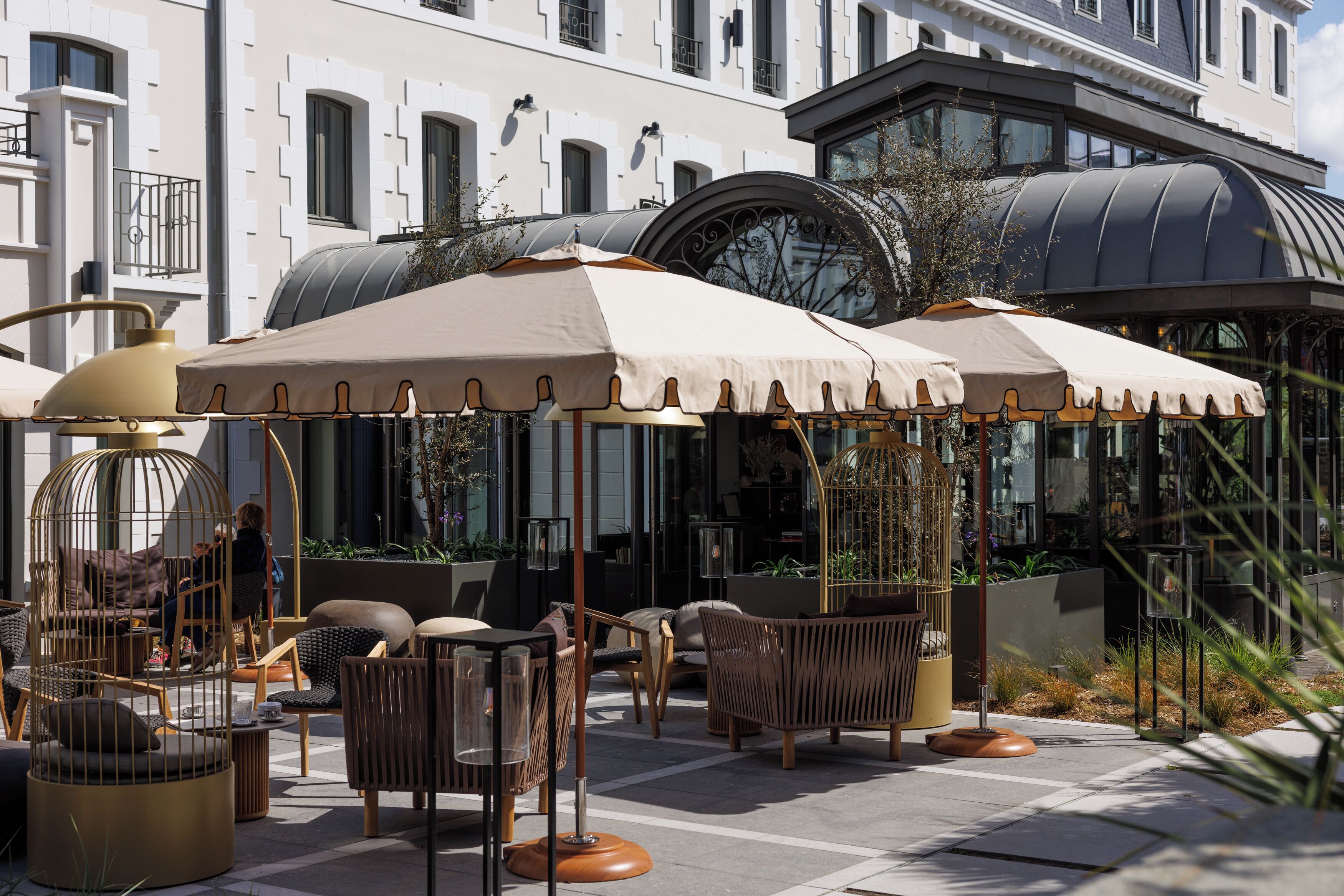 Outdoor seating with umbrellas, wicker furniture, and a building with large windows in the background.