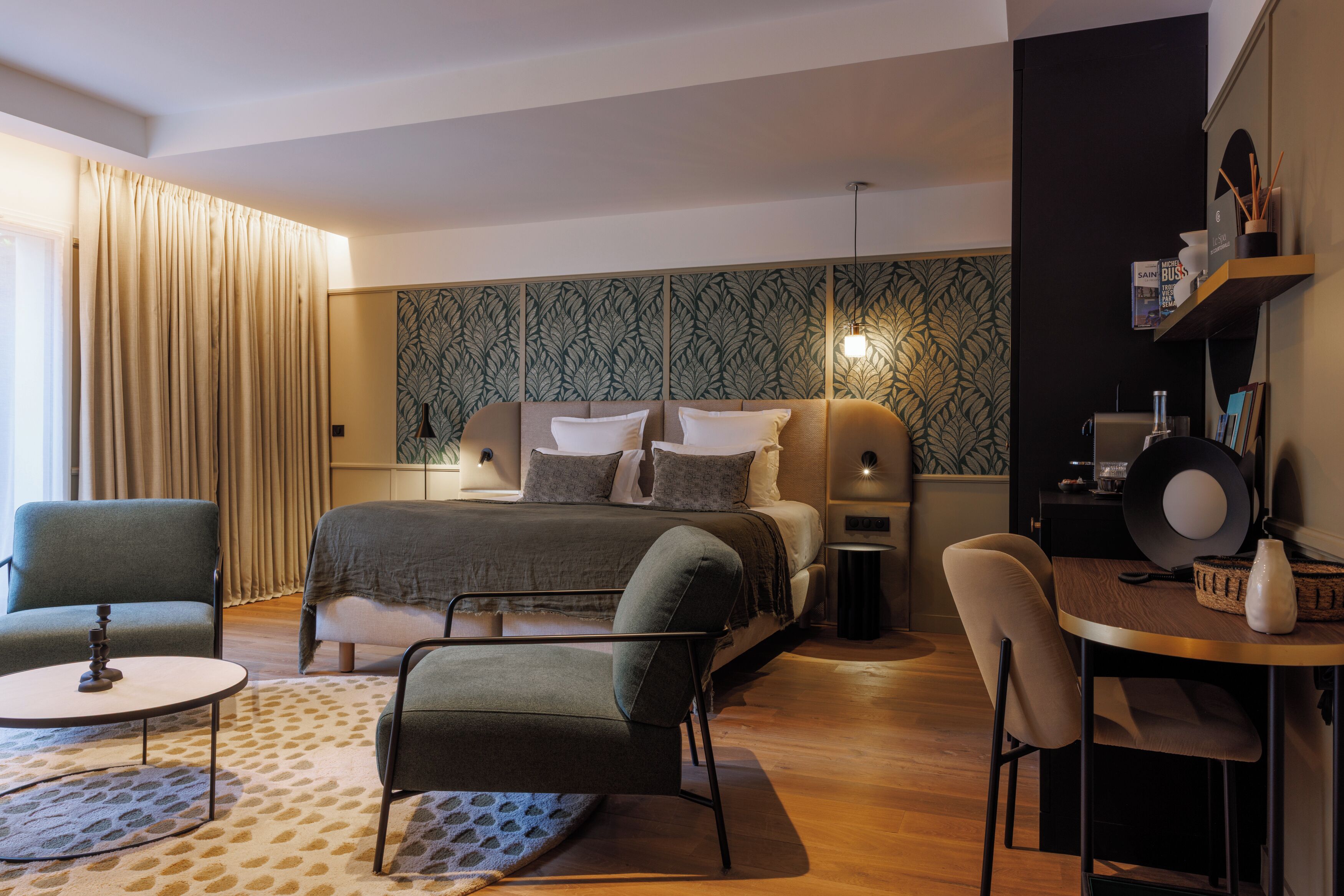 A modern bedroom with a bed, two chairs, a small table, and a desk.