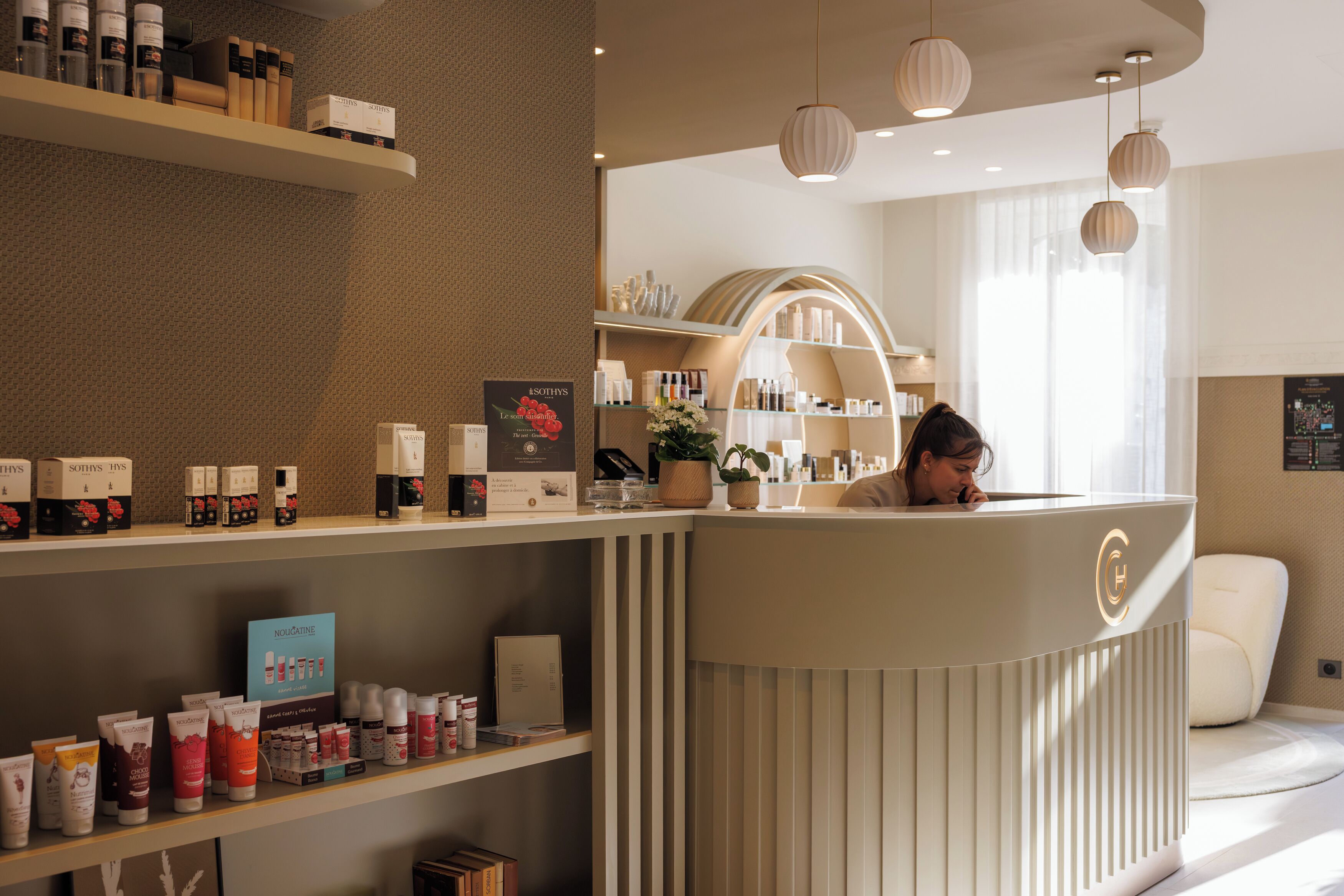 A reception area with a counter, shelves with products, a potted plant, and a window with curtains.