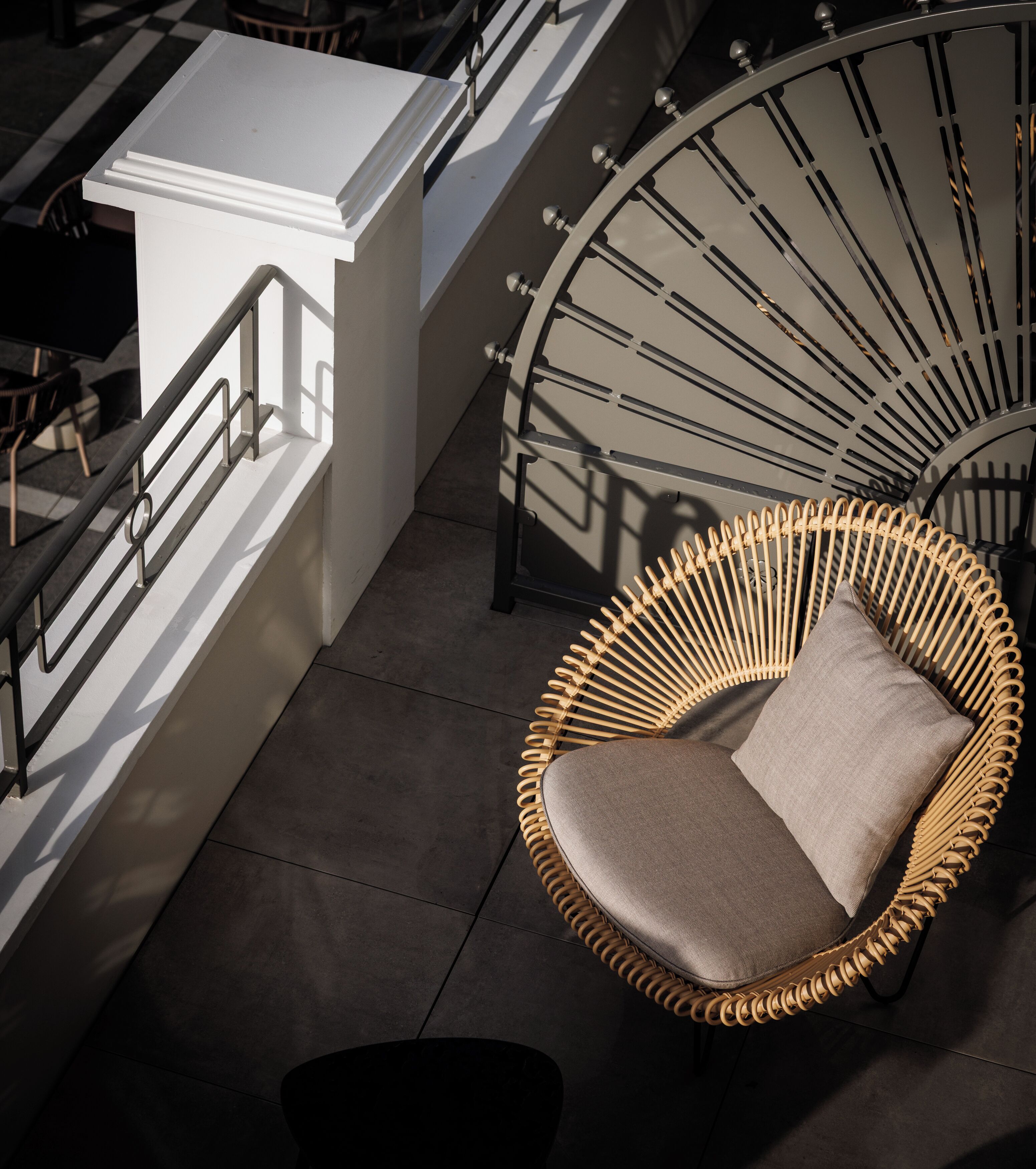 A wicker chair with a cushion on a tiled floor, a white railing, and a staircase with a metal handrail.