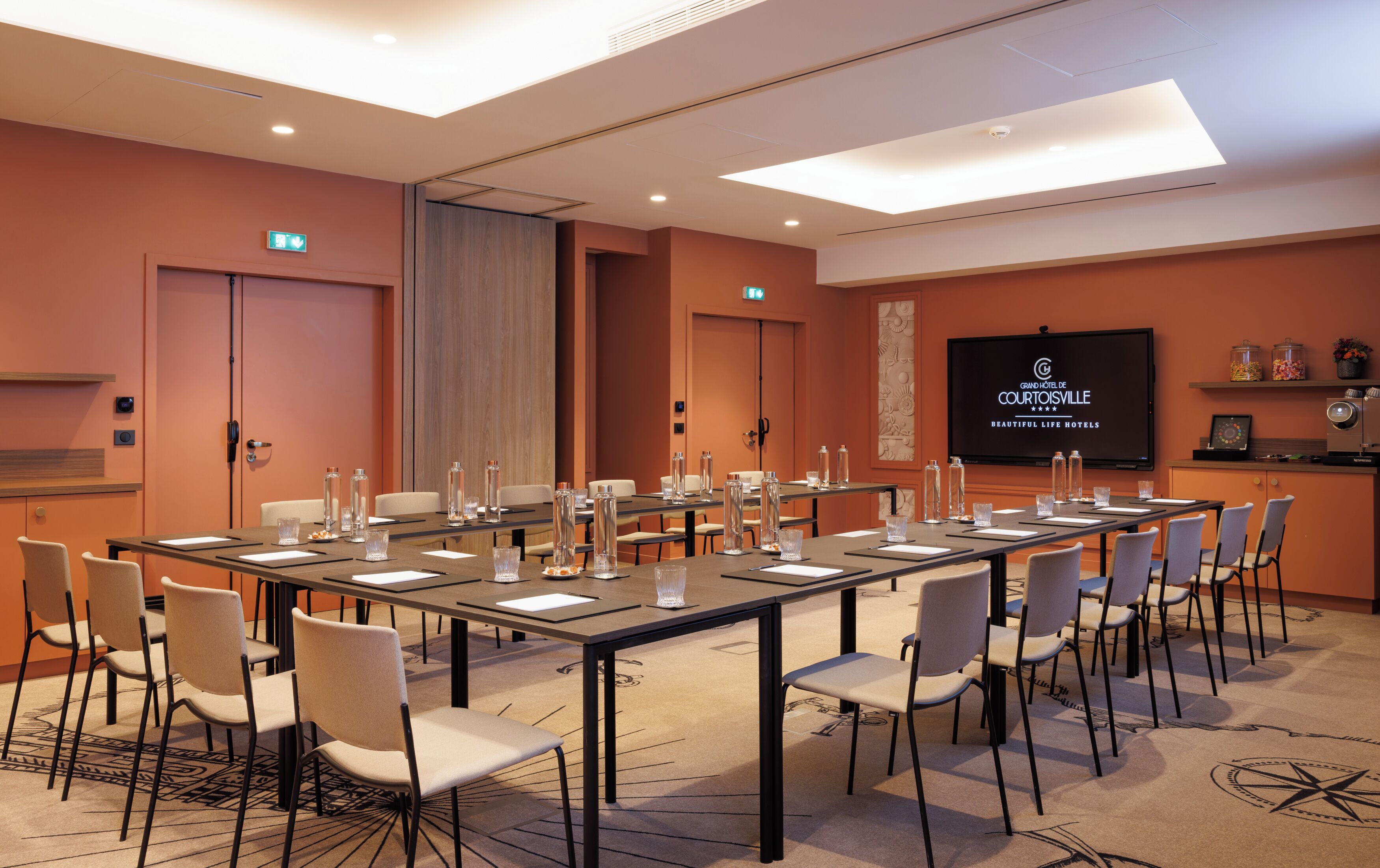 A conference room with a long table, chairs, and a television screen displaying the hotel name.