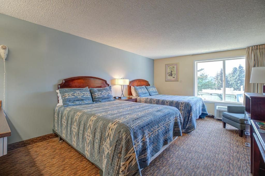 A hotel room with two beds, a desk, a chair, a lamp, and a window with a view.