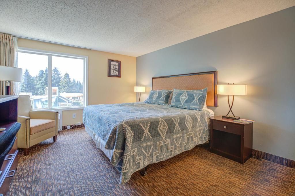A hotel room with a bed, two bedside lamps, a chair, a desk, and a window with a view.
