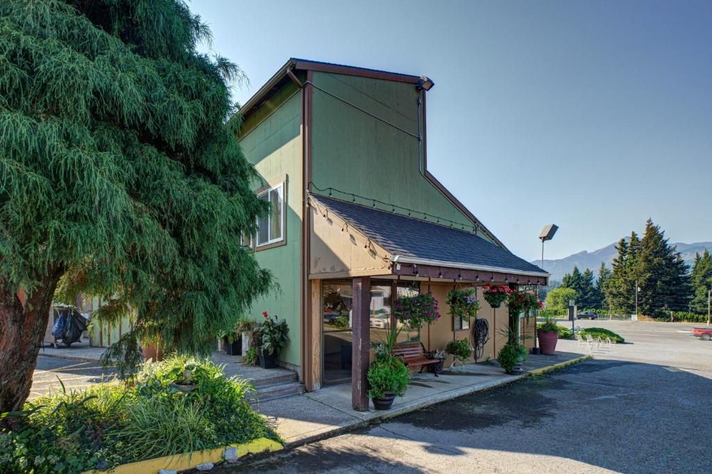 A two-story building with a green facade, a covered porch with potted plants, and a mountain backdrop.