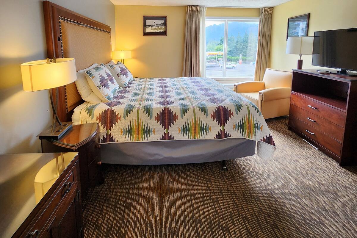 Habitación de hotel con cama, escritorio, silla, televisor y ventana con vistas a montañas.