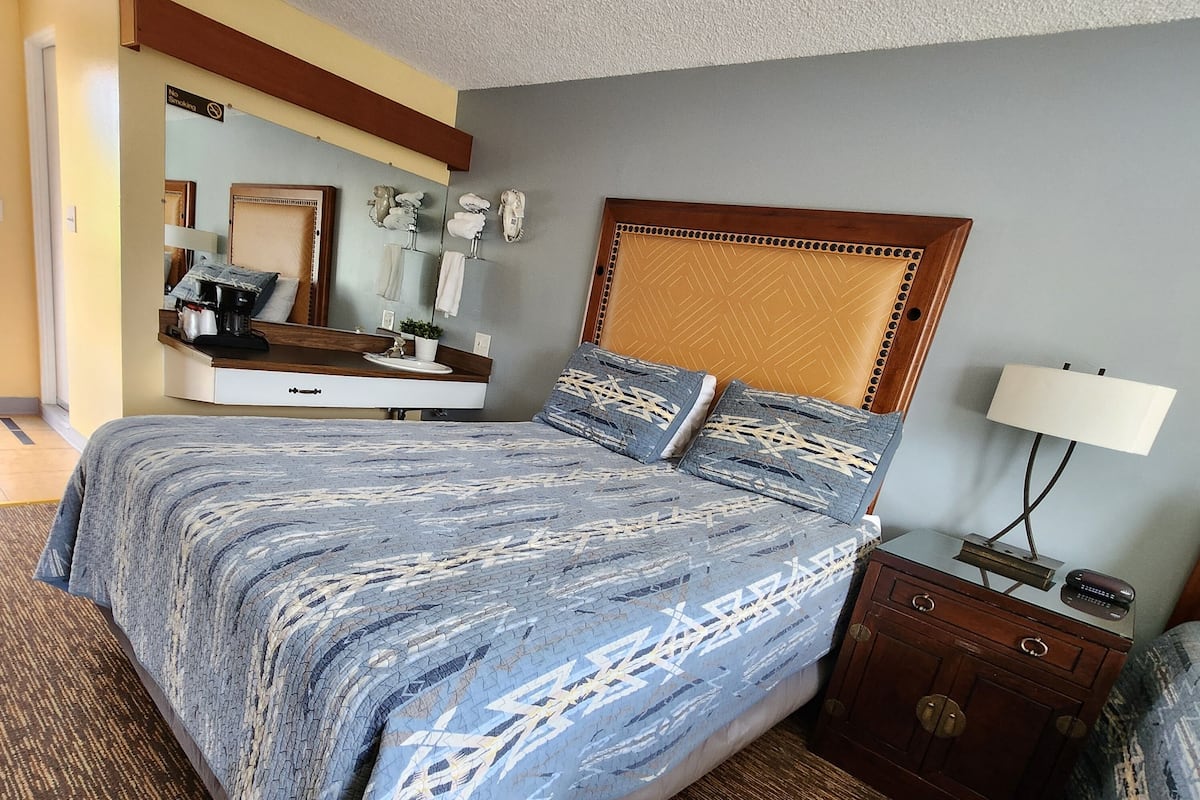 Una habitación de hotel con una cama grande, una mesita de noche, un tocador, un espejo y una lámpara.
