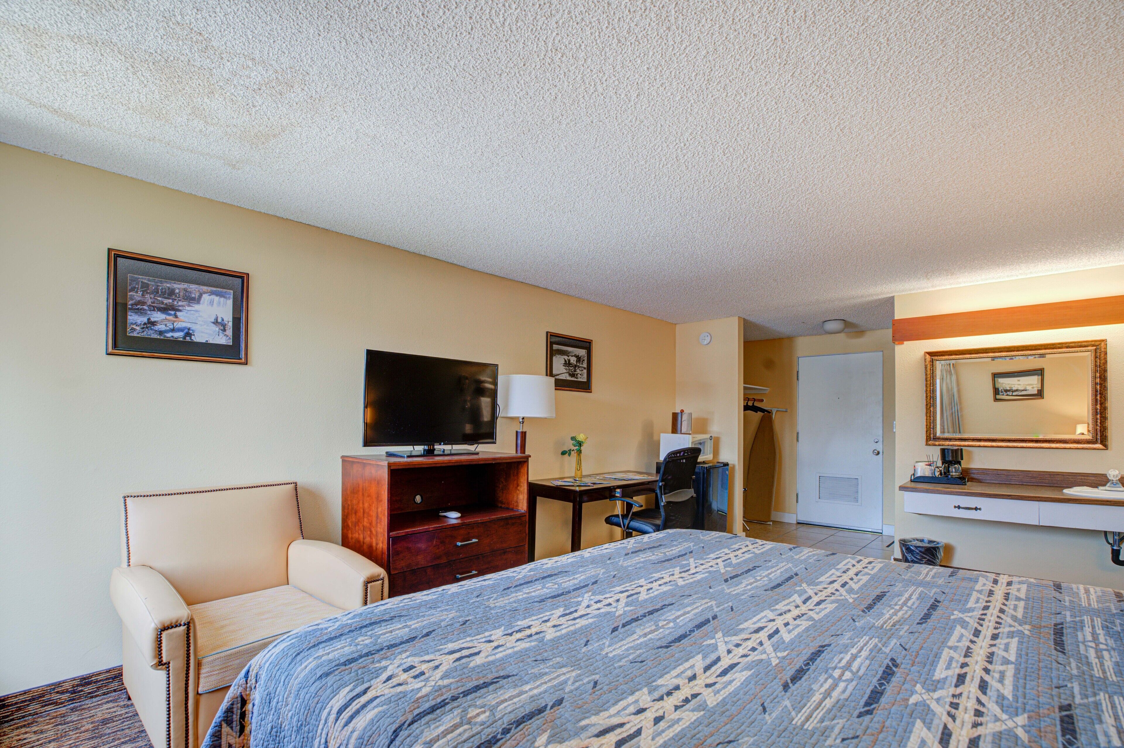 Une chambre d’hôtel équipée d’un lit, d’une télévision, d’un bureau, d’une chaise et d’une salle de bain visible à travers une porte ouverte.