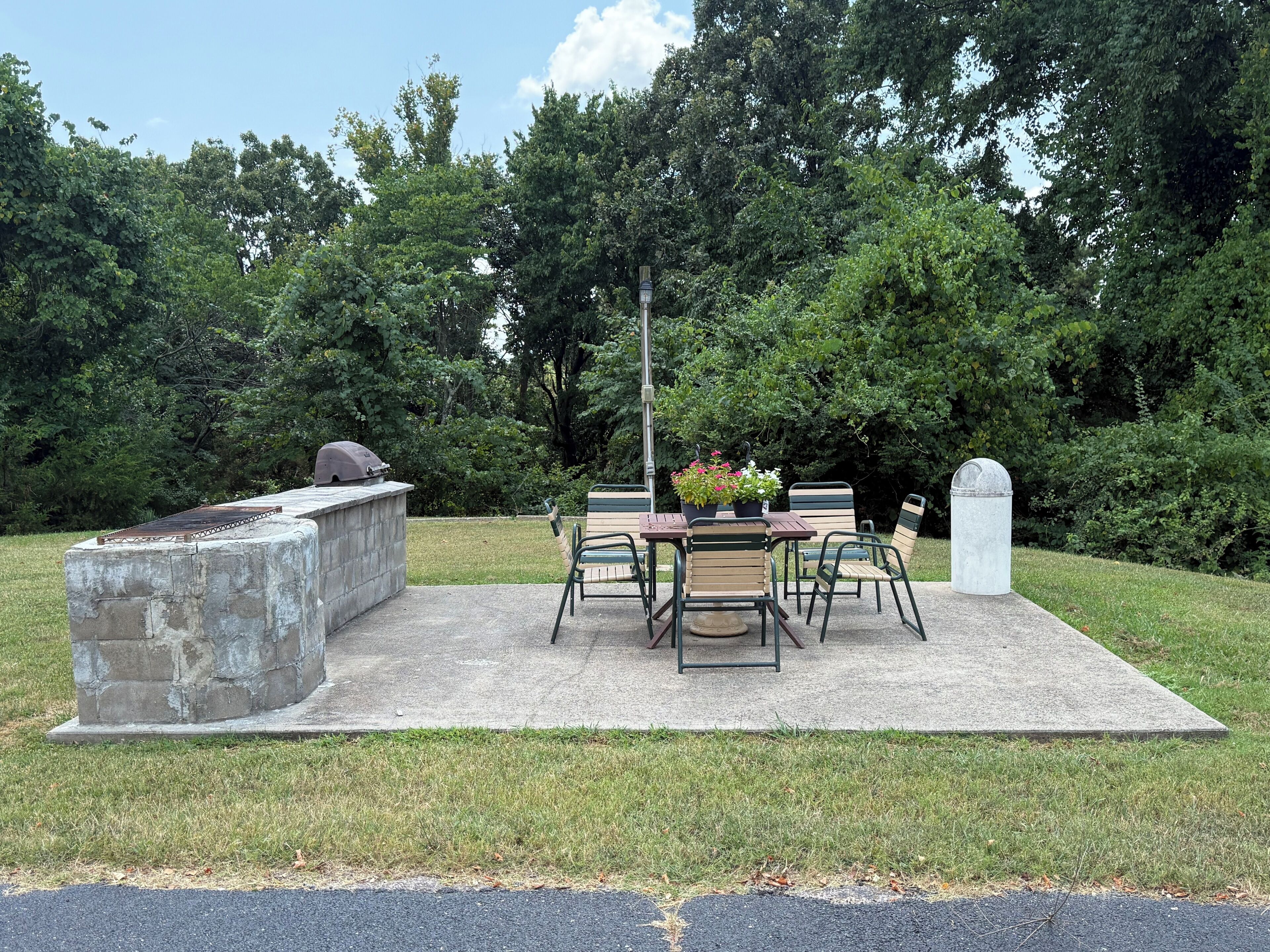 An outdoor patio with a barbecue grill, a table with chairs, and a stone planter with flowers.