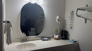 A bathroom with a round mirror, three wall-mounted lights, a towel rack, a hairdryer, a coffee maker, and a basket with toiletries. - Wagner Inn (Eureka Springs)