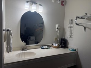 A bathroom with a round mirror, three wall-mounted lights, a towel rack, a hairdryer, a coffee maker, and a basket with toiletries. - Wagner Inn (Eureka Springs)