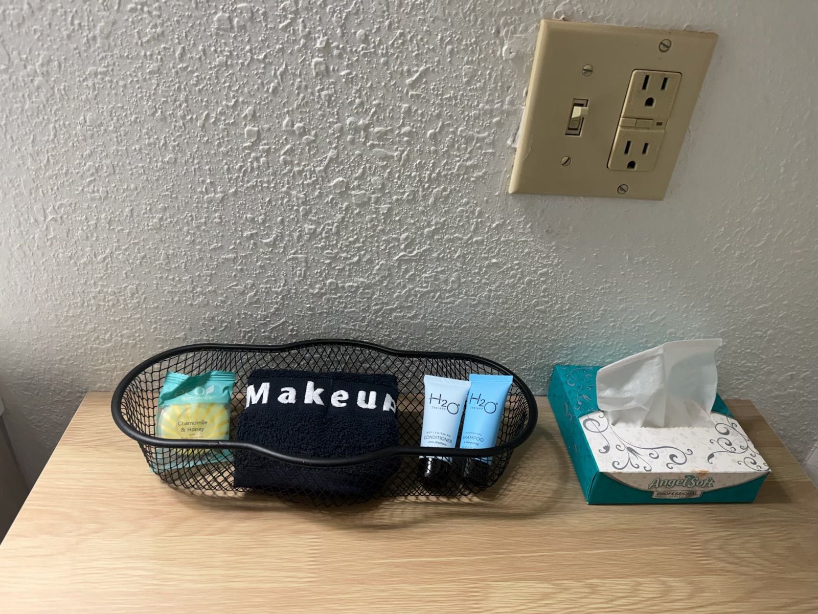 A black mesh organizer with makeup items on a wooden table.